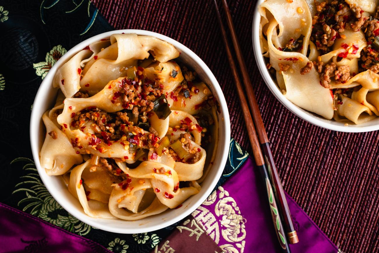 Image of thick, pulled noodles called biang biang from Xian, China, in a bowl with chopsticks set to the side